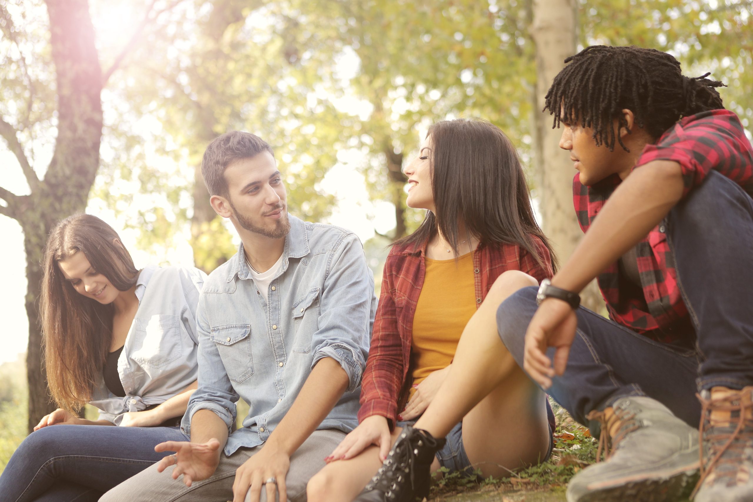 4 personas jóvenes conversando sentadas en el pasto