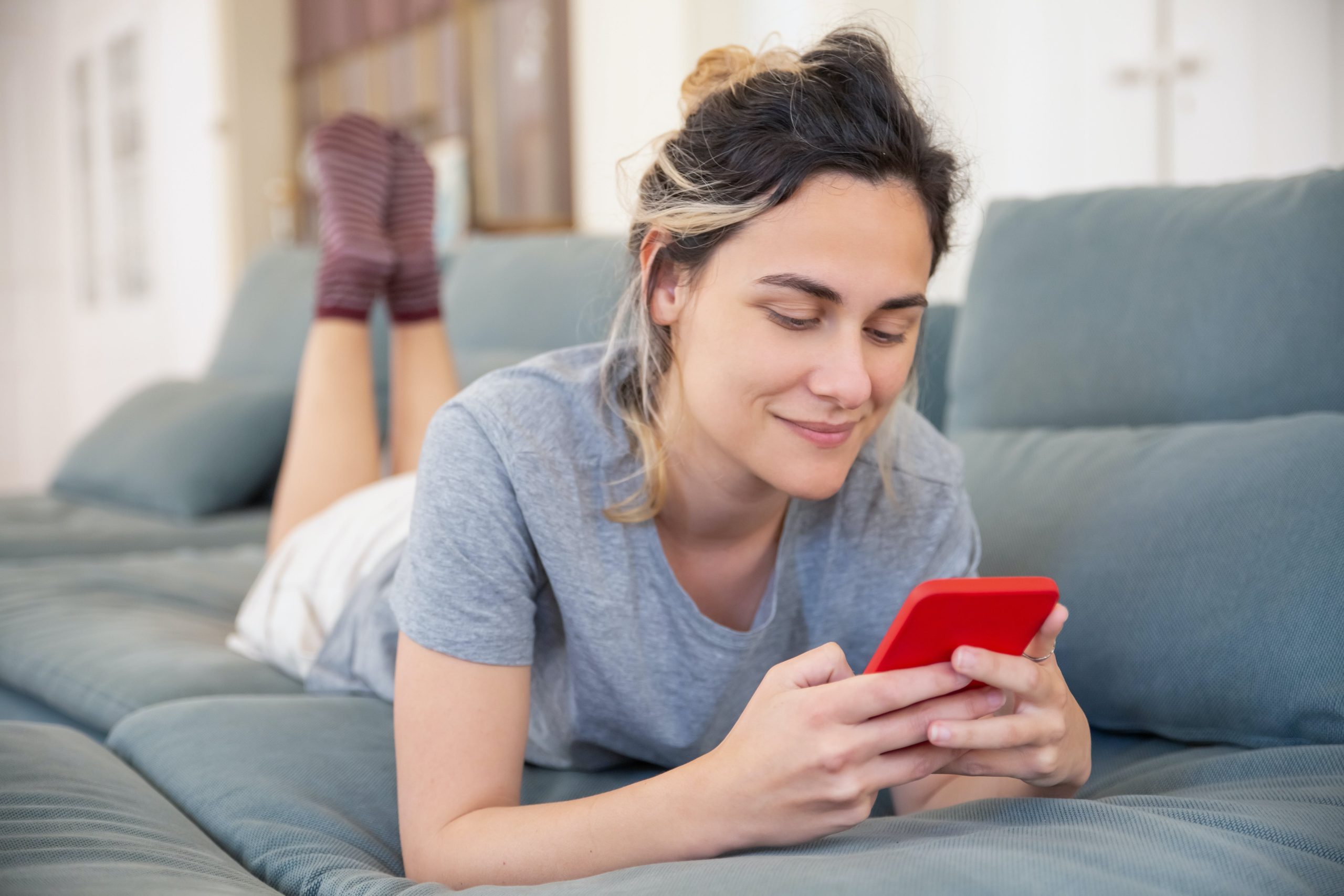 Mujer mirando su smartphone recostada sobre el sofá