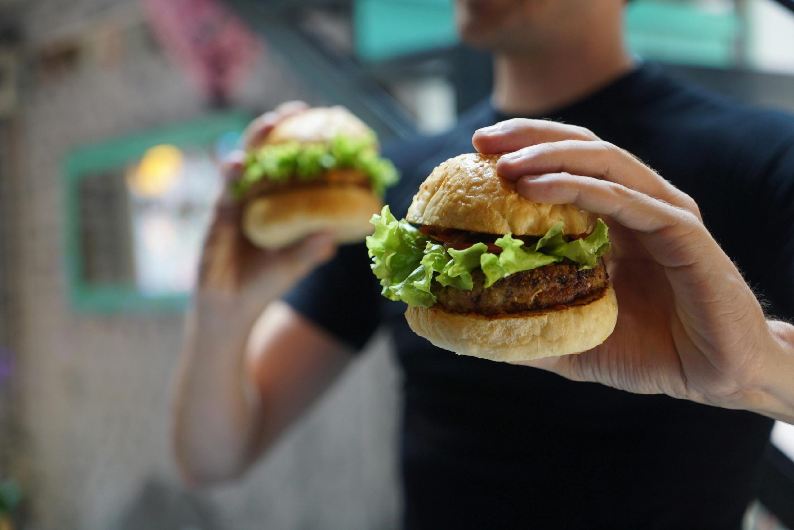 Hombre sosteniendo dos hamburguesas una para él y ofreciendo la segunda